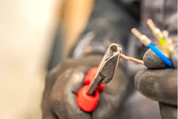 Gloved hands use red pliers to cut copper wire, surrounded by insulated cables.