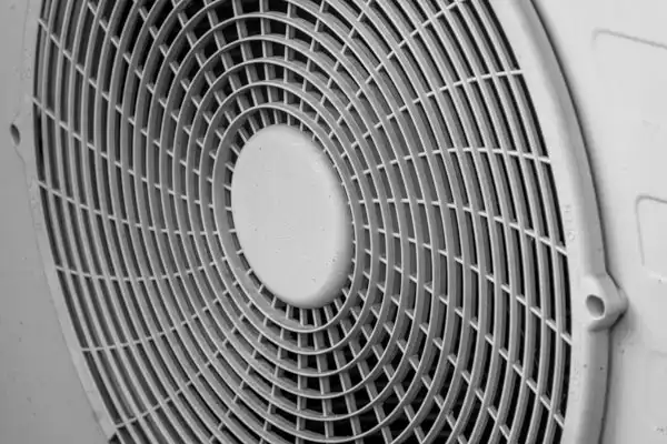 Close-up view of a circular fan grille with a grid pattern, covering the blades of a ventilation or cooling device.